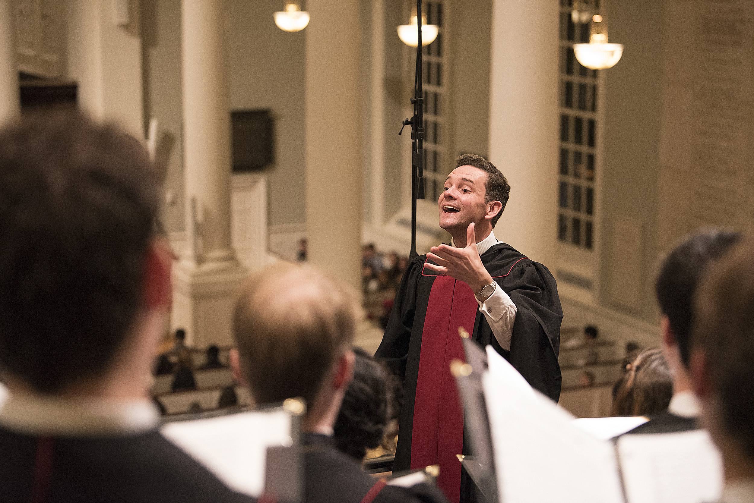 Choirmaster faces singers with raised hand.