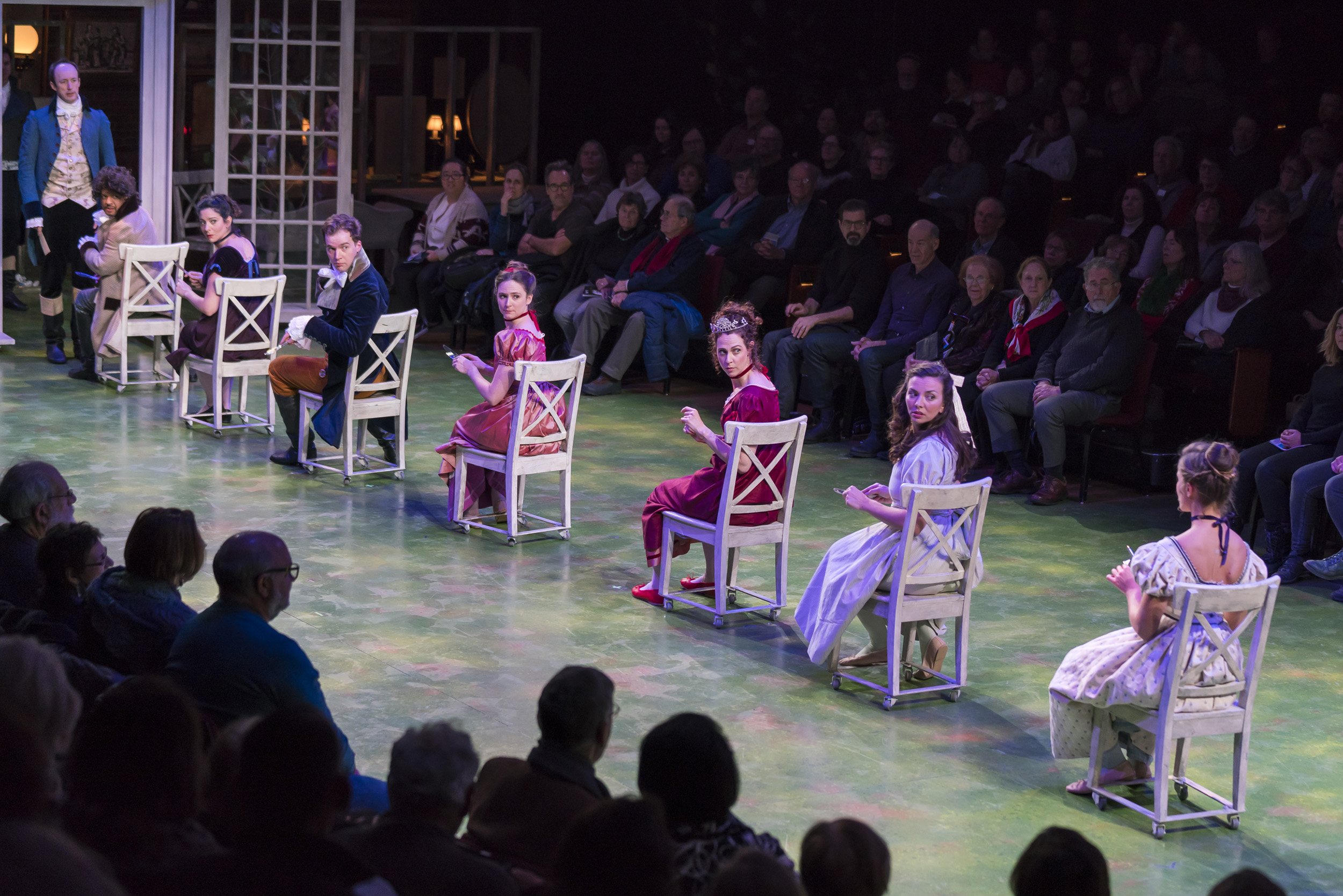 Actors sit in chairs lined up across the stage.