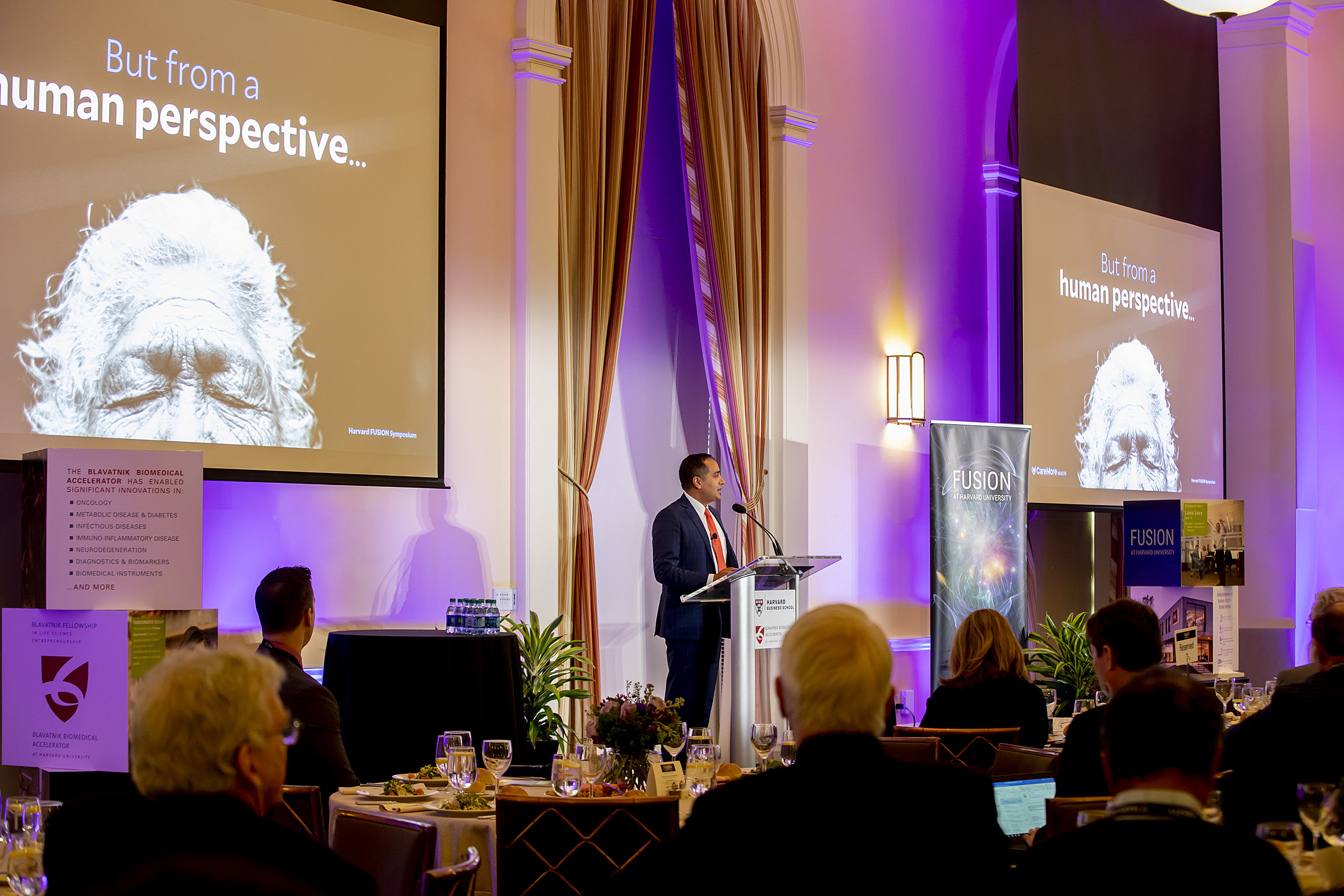 A man at a podium with big projection screens on either side of him