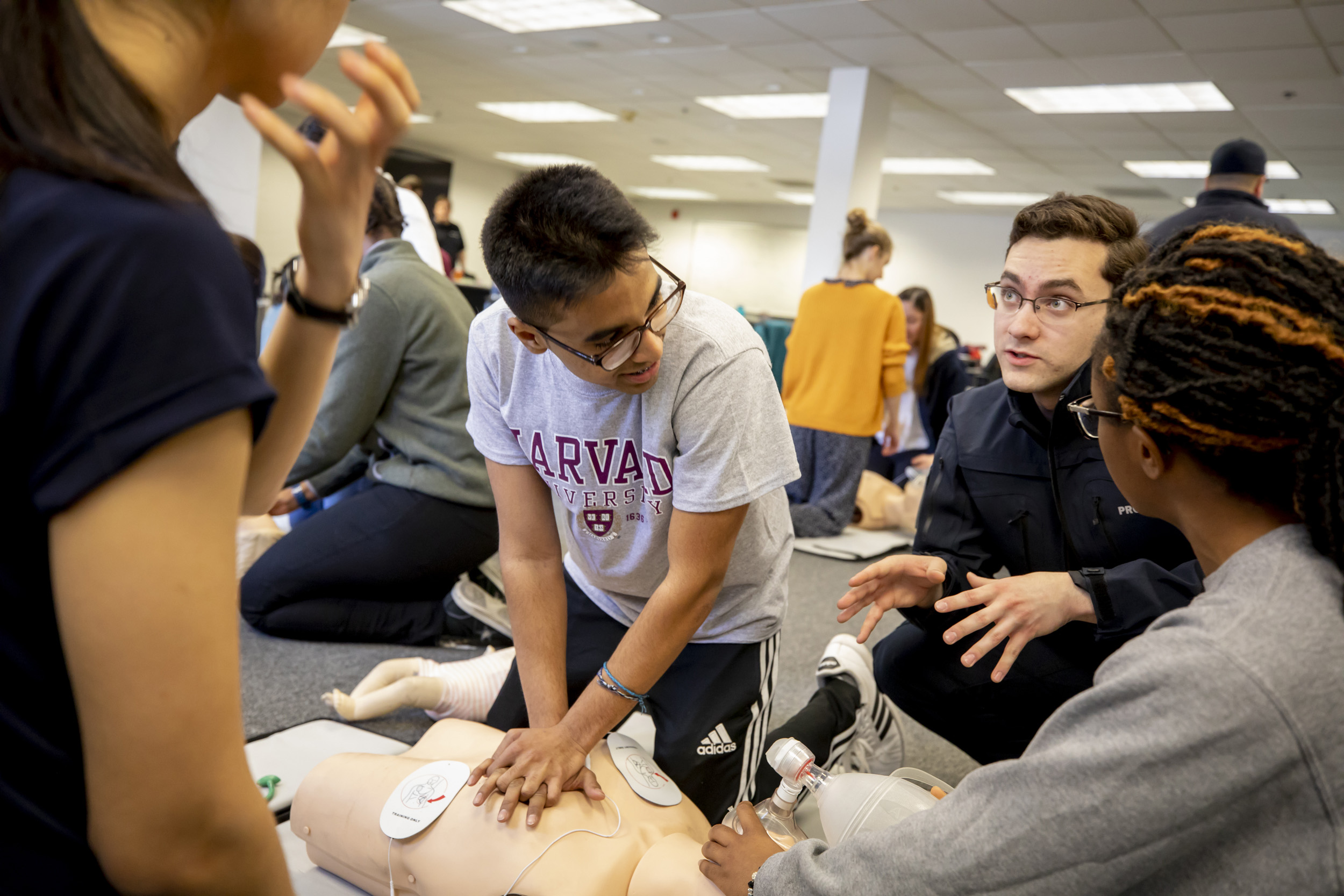 An instructor helps students performing CPR on a dummy.