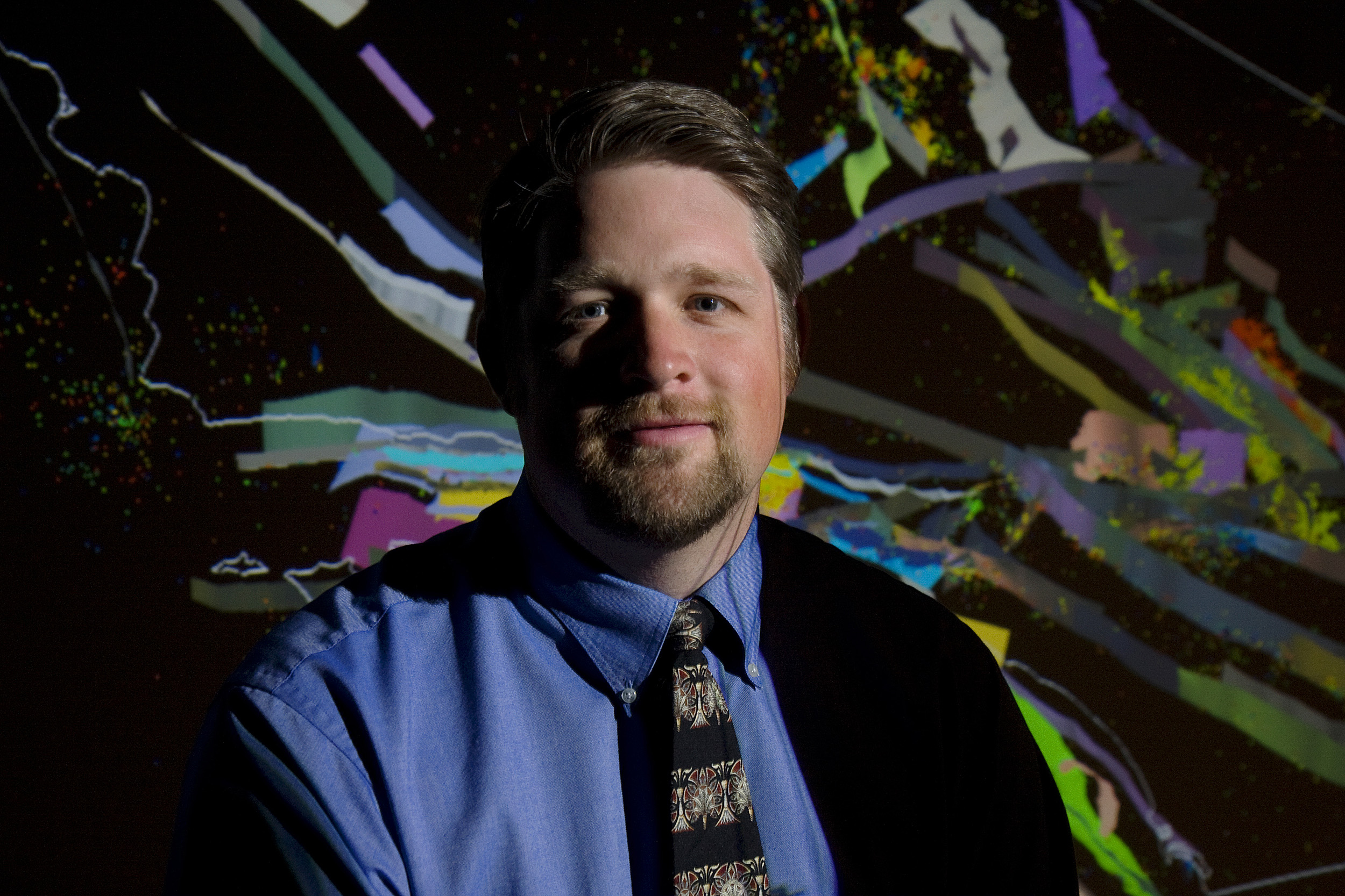 John Shaw against a black and rainbow background