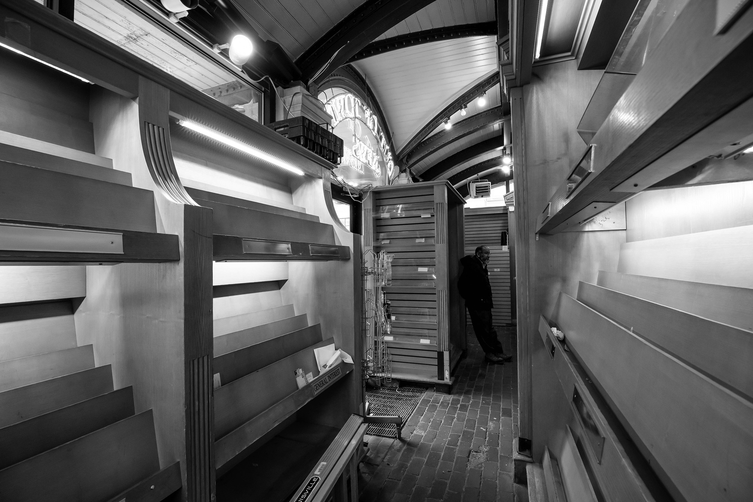 Black and white image of emptied newspaper and magazine stands in Out of Town News.