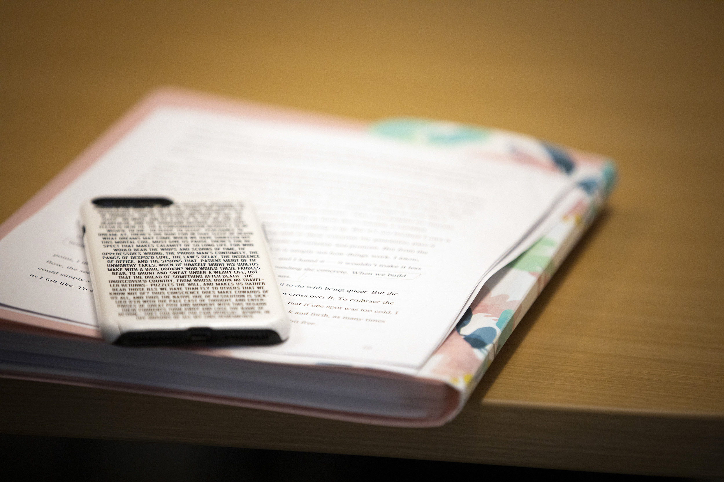 A smart phone decorated with text from Shakespeare's Hamlet sits on writing materials during class.