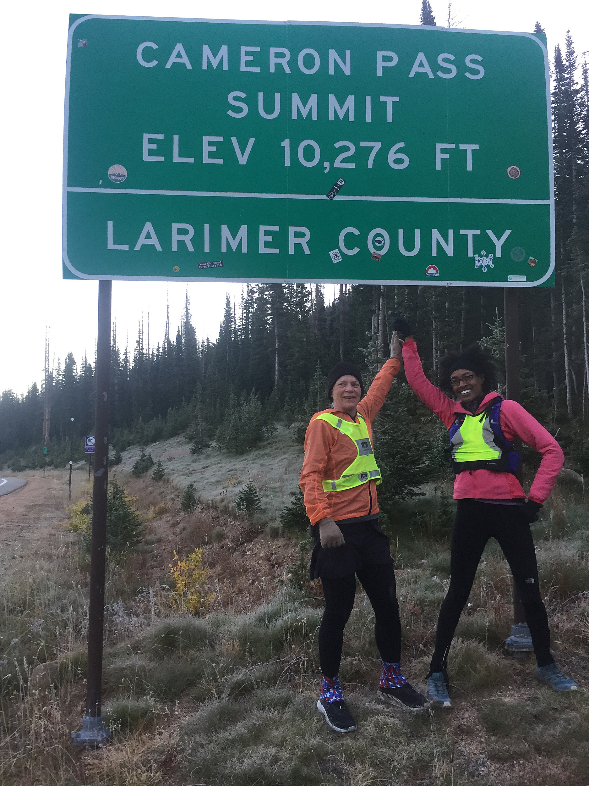 Two women hold hands triumphantly under landmark sign.