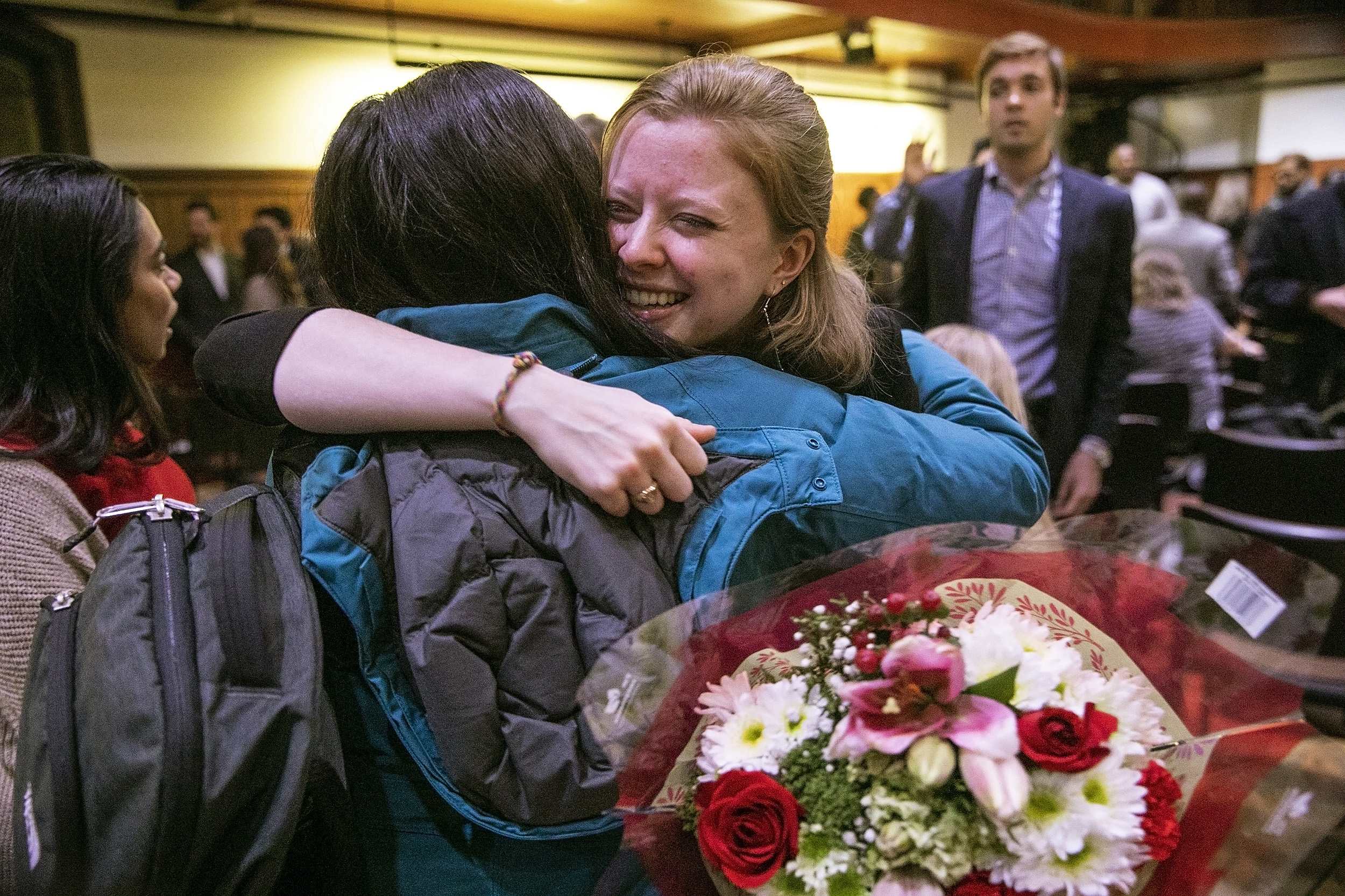 Graduates hugging with flowers in hand.