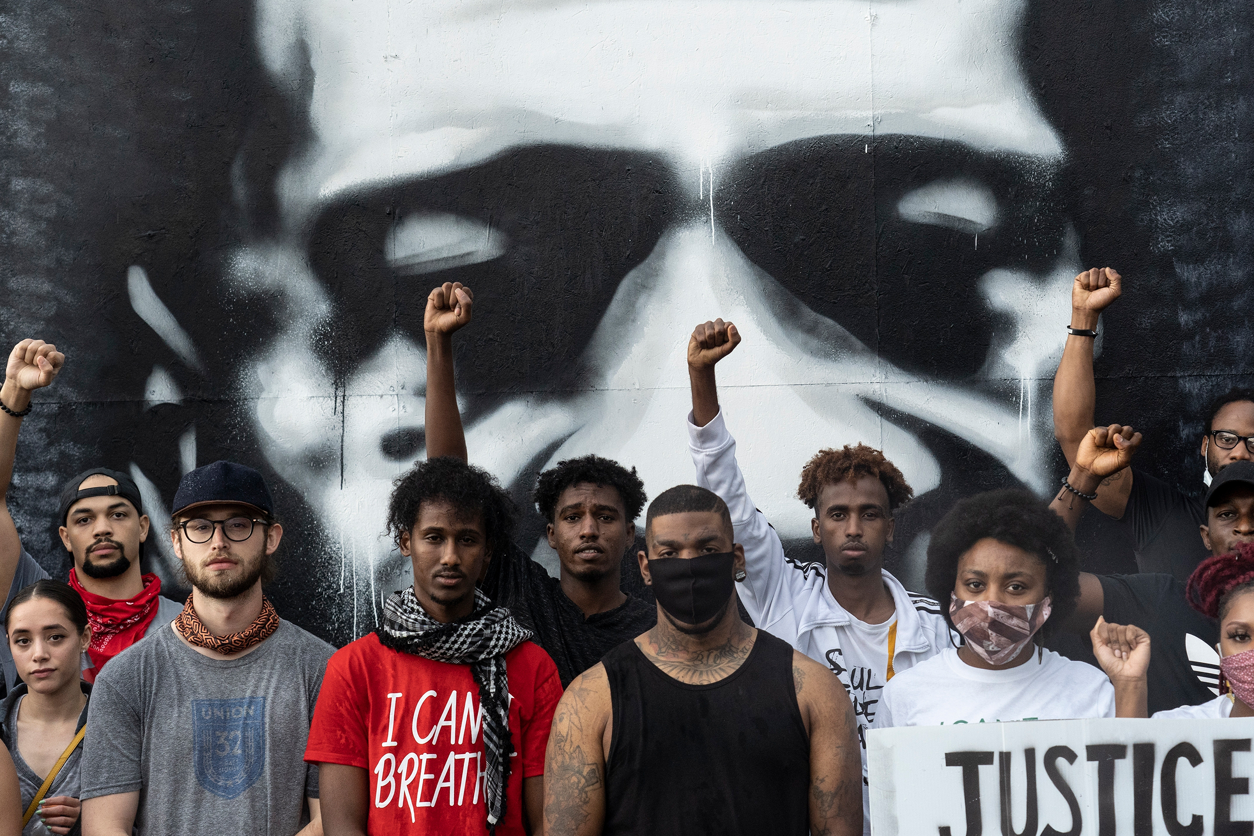 People pose in front of a mural of George Floyd