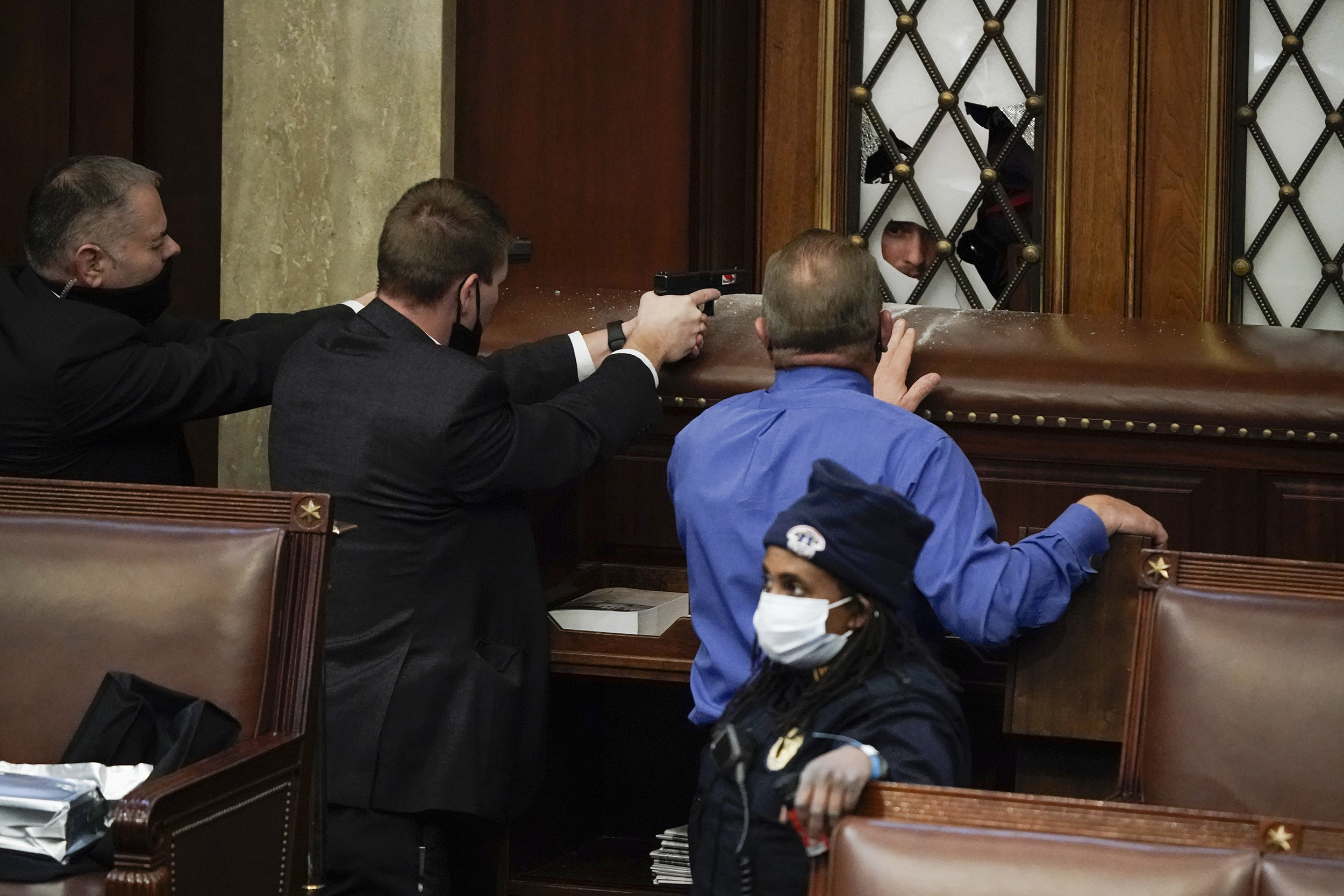 Police with guns drawn watch as rioters try to break into the House Chamber.