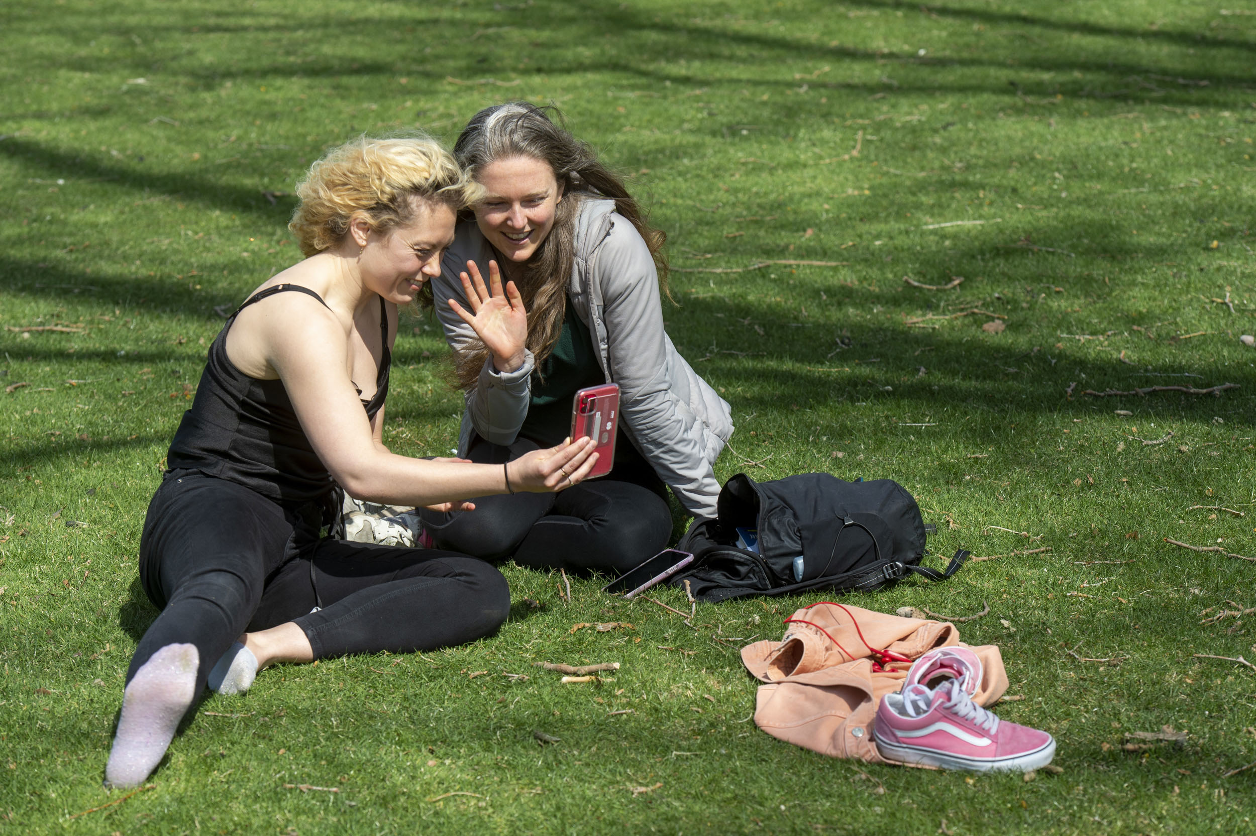 Grace Birch and Whitney McFadden FaceTime with a friend while relaxing on the HKS lawn adjacent to Memorial Drive.