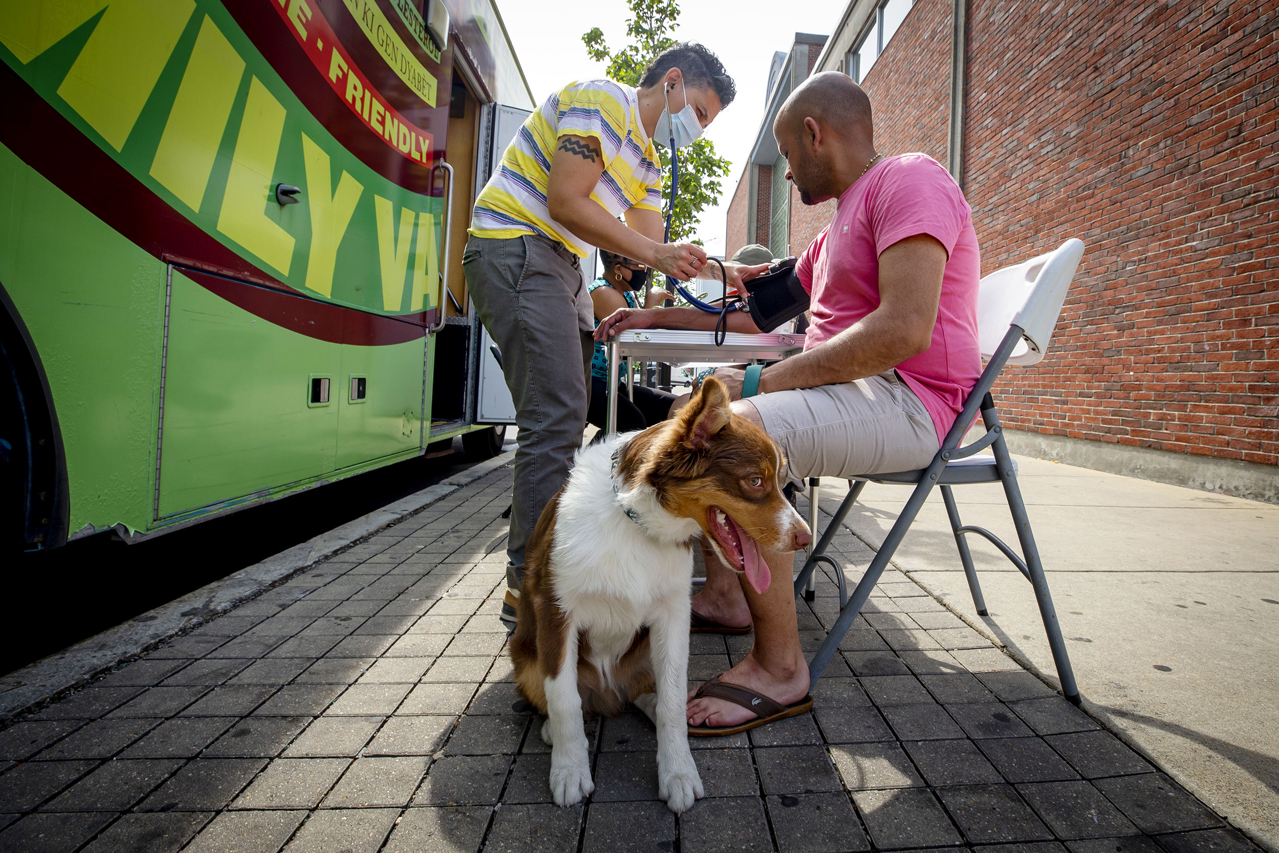 Staffer, Simone de Oliveira, left administers a blood pressure test to Fabio Echeveri of E. Boston while his dog Benji, waits at Harvard University's Family Van.