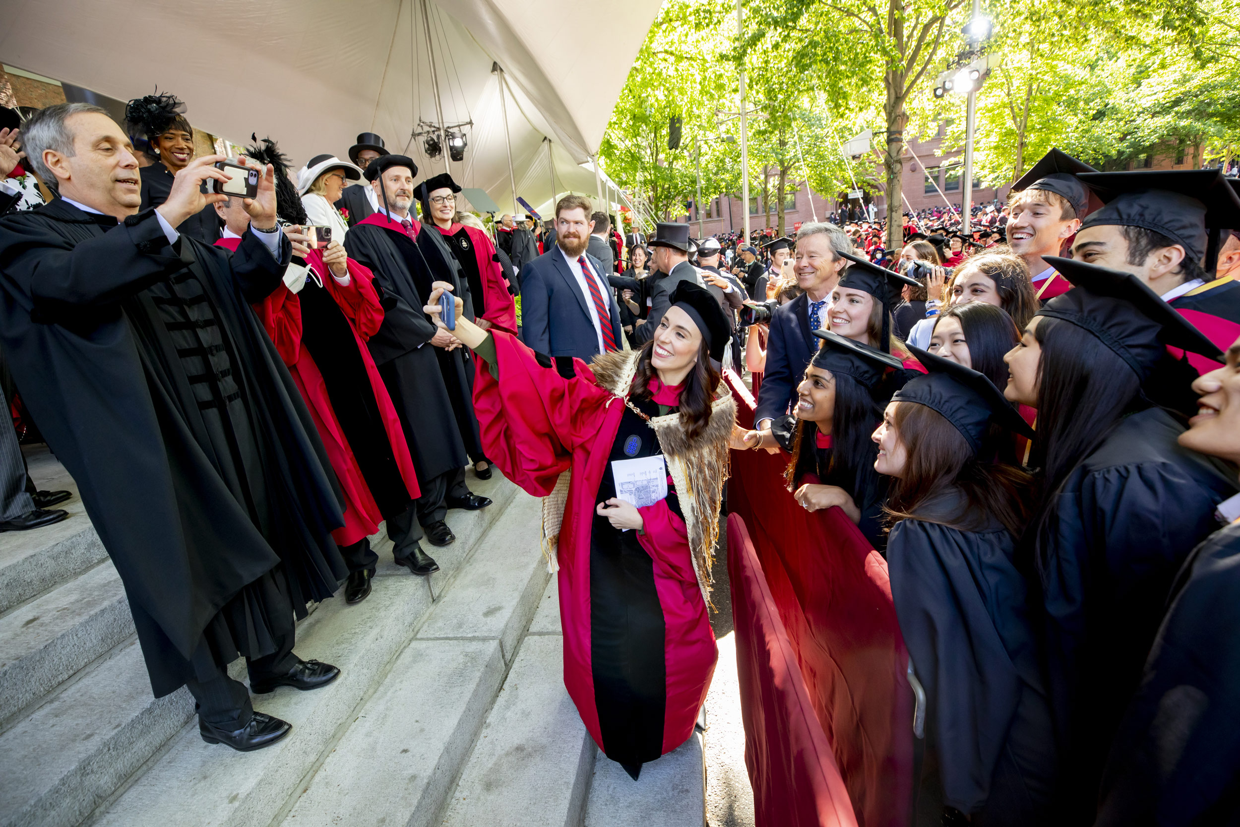 Harvard University President Larry Bacow and New Zealand Prime Minister Jacinda Ardern take photos with graduates before the ceremony begins.