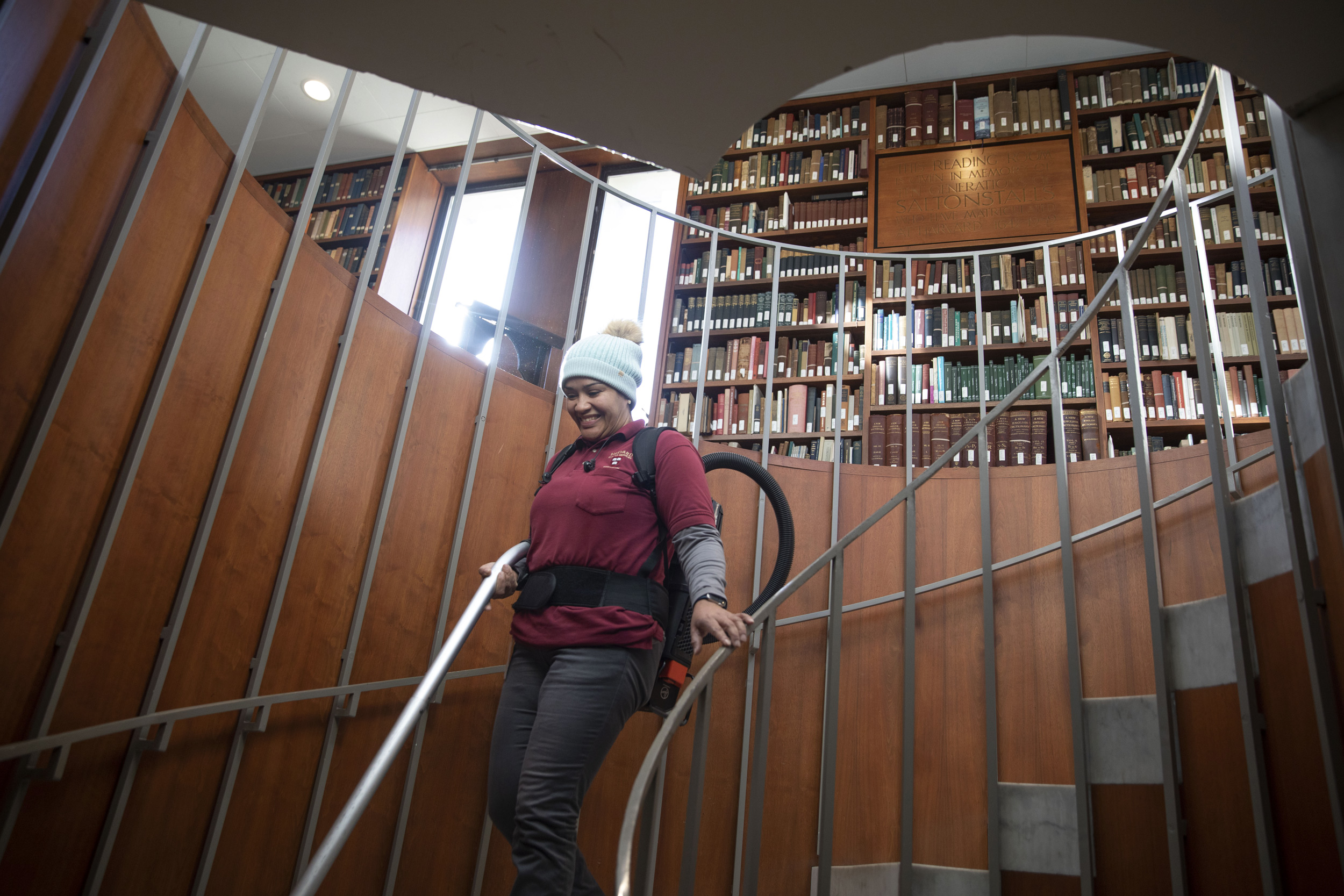 Evelyn Pena walks down the spiral staircase while cleaning the Leverett House Library.