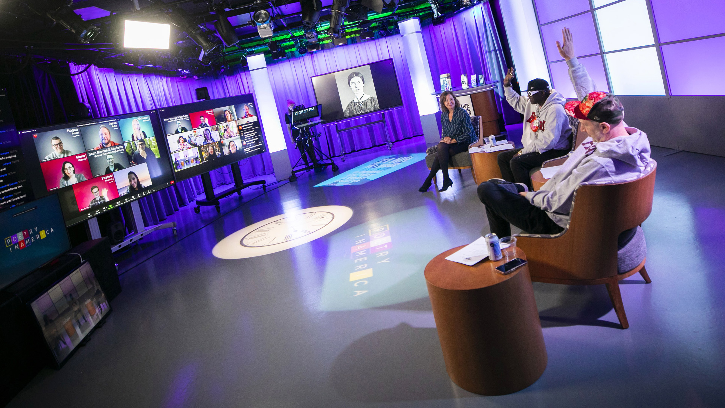 Elisa New, Flavor Flav, and Sam Hollander sit in studio facing screens showing students attending session virtually.