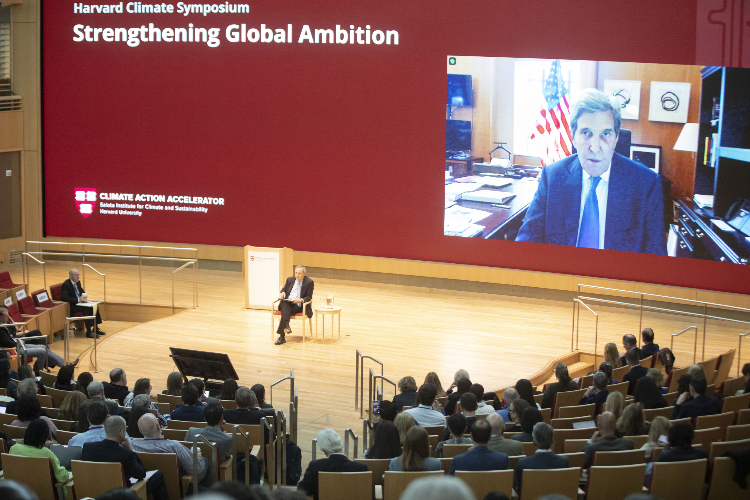 John Kerry on screen in conversation with Larry Bacow.