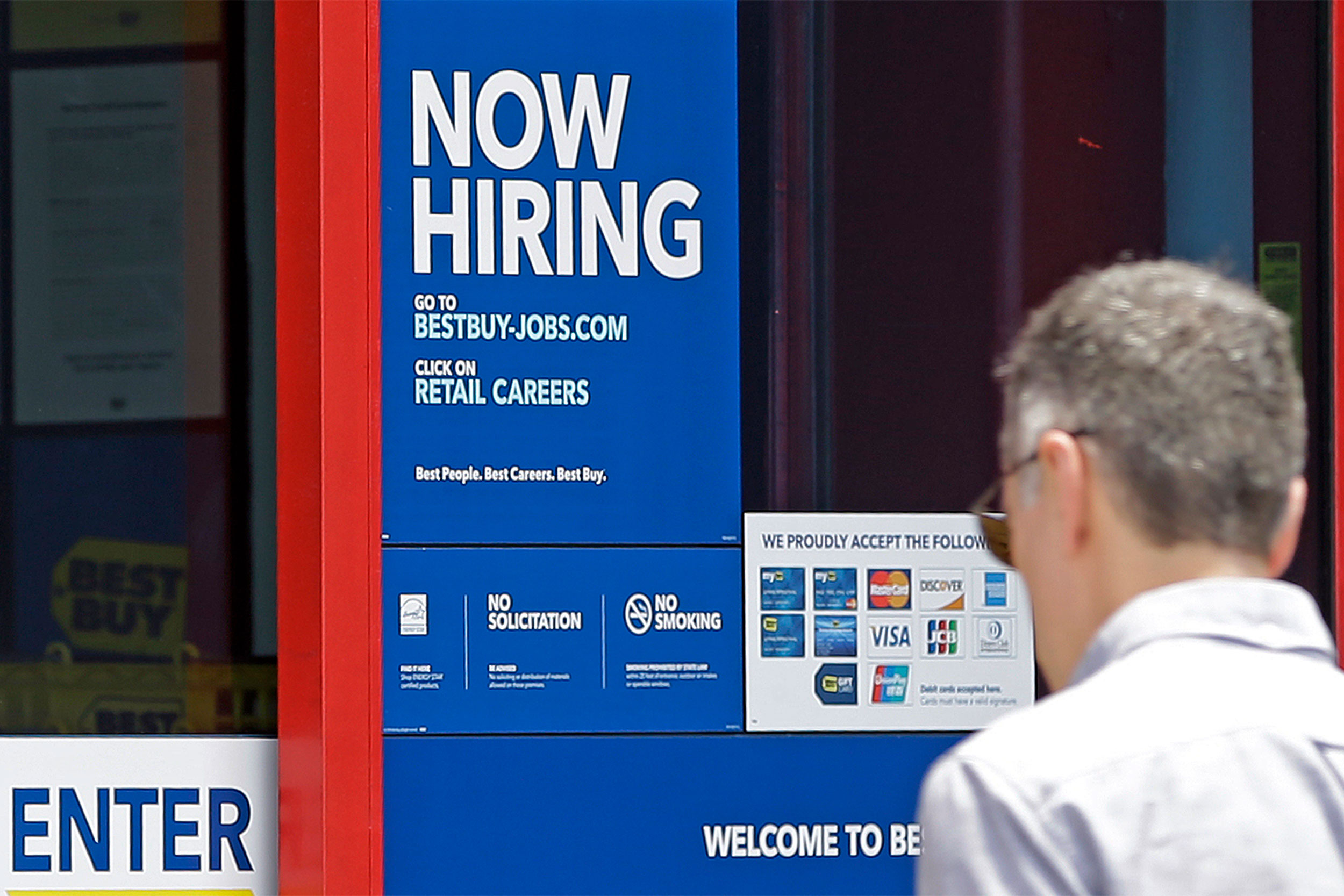 Man looking at "Now Hiring" sign.