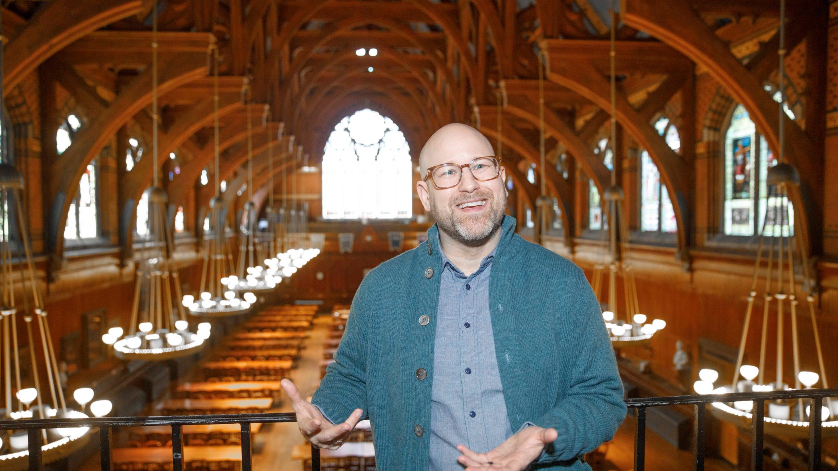 Greg Epstein wearing glasses, a button up shirt, and knit cardigan. 