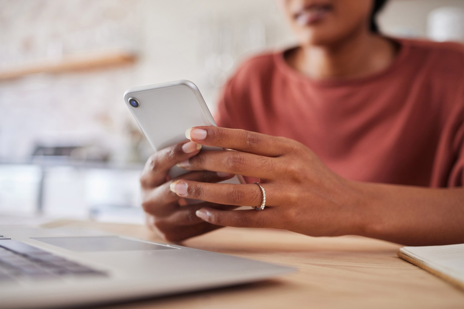 Woman with wedding ring holding smartphone and looking at computer.