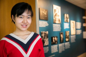 Xue (Snow) Dong in front of the photo wall in Currier House