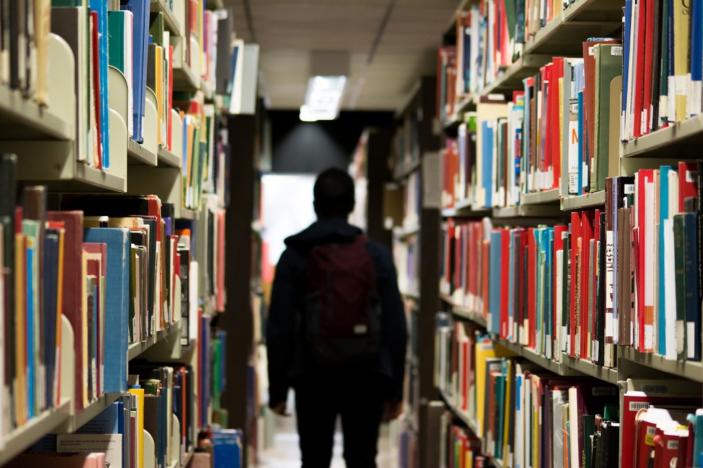 A person in silhouette between library book shelves