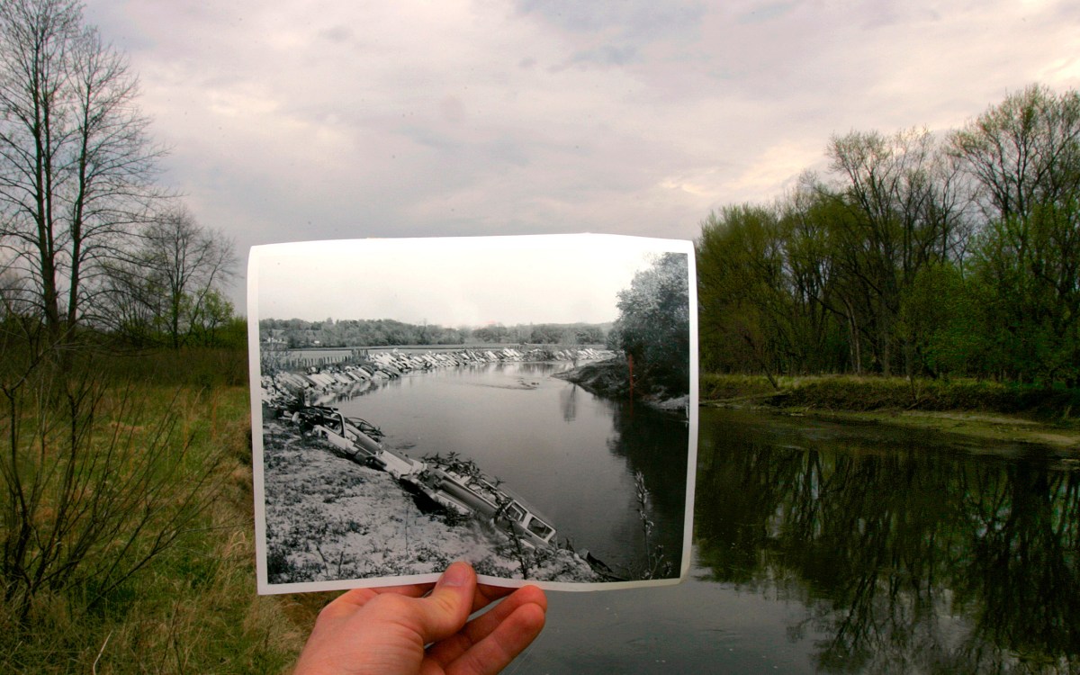 A 1967 photograph, showing old cars used as rip-rap along the banks of the Cuyahoga to protect it from erosion is held in front of the river decades later.