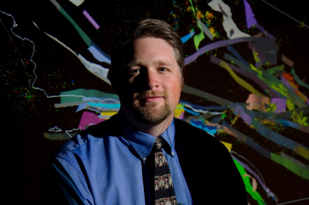 John Shaw against a black and rainbow background