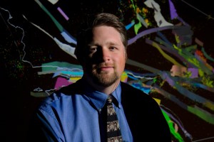 John Shaw against a black and rainbow background