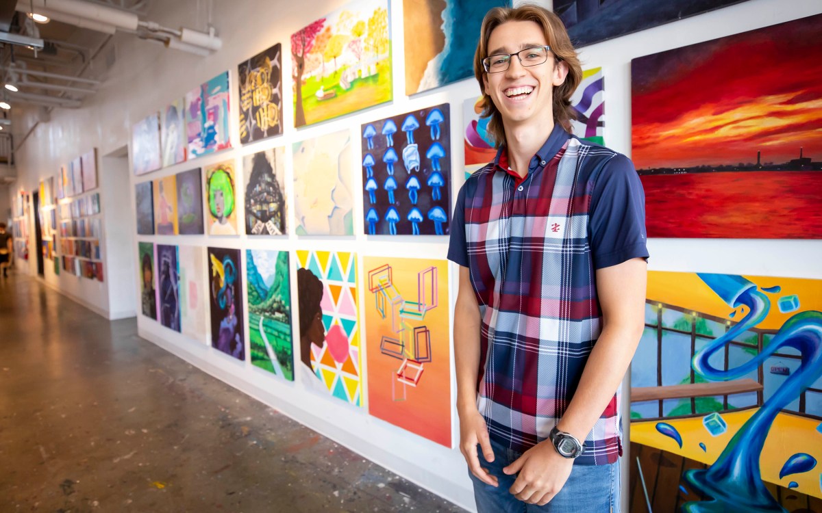 Harvard first year student standing in front of student artwork on wall.