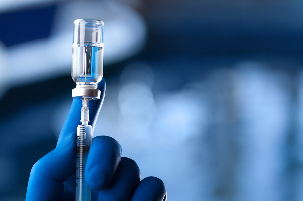 A medical hand in a glove holds an ampoule with a vaccine and a syringe with illustration