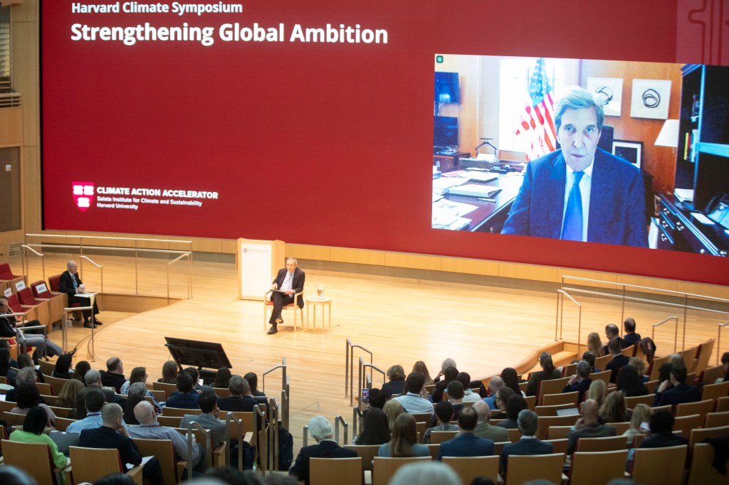 John Kerry on screen in conversation with Larry Bacow.