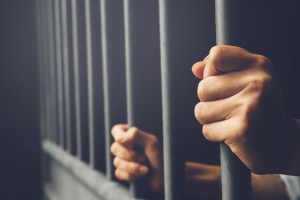 Person holds bars of jail cell.