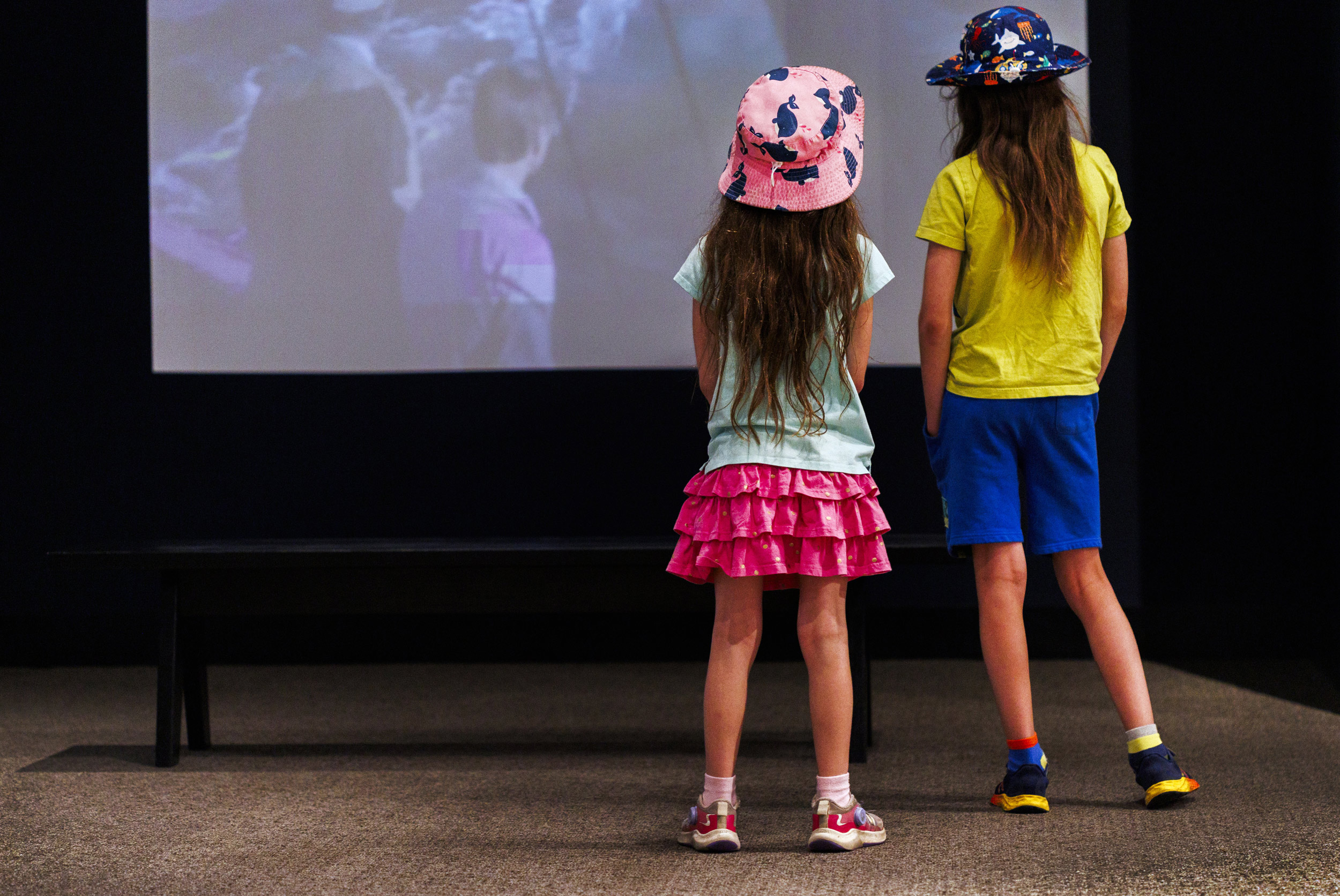 Young visitors from the community Coral and Alexander Ain watch a projection of the film Jaws within the exhibit.