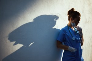 woman doctor standing in the shadows with her head tilted down.