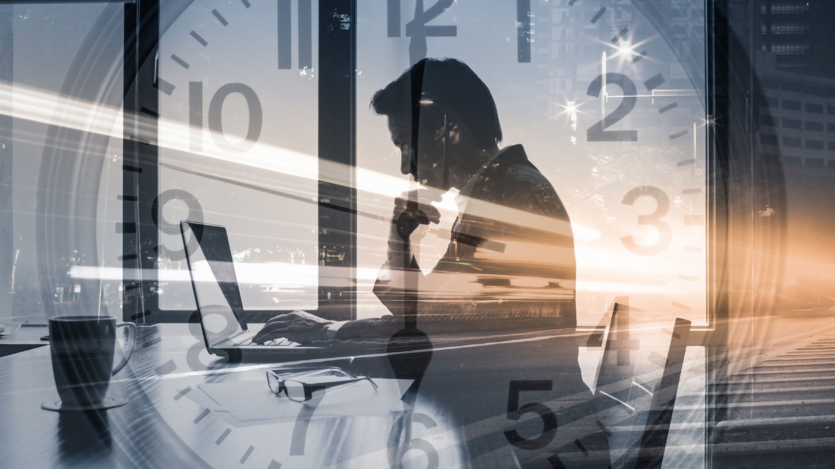 Businessman sitting at desk and working with clock in background