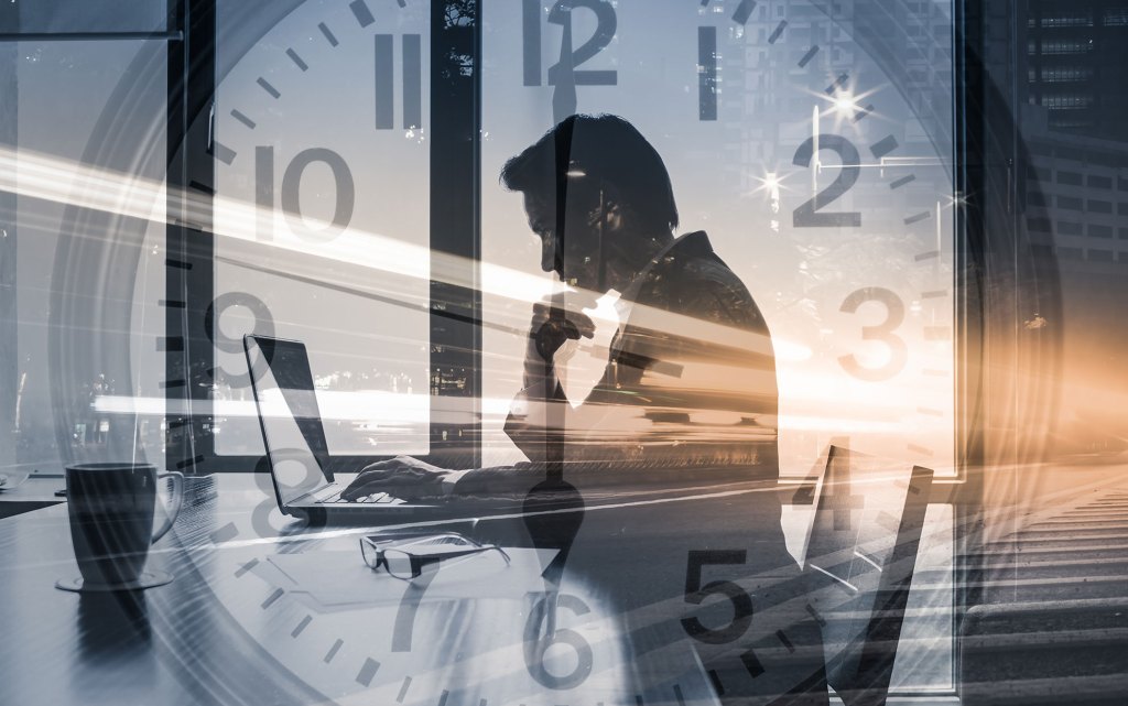 Businessman sitting at desk and working with clock in background