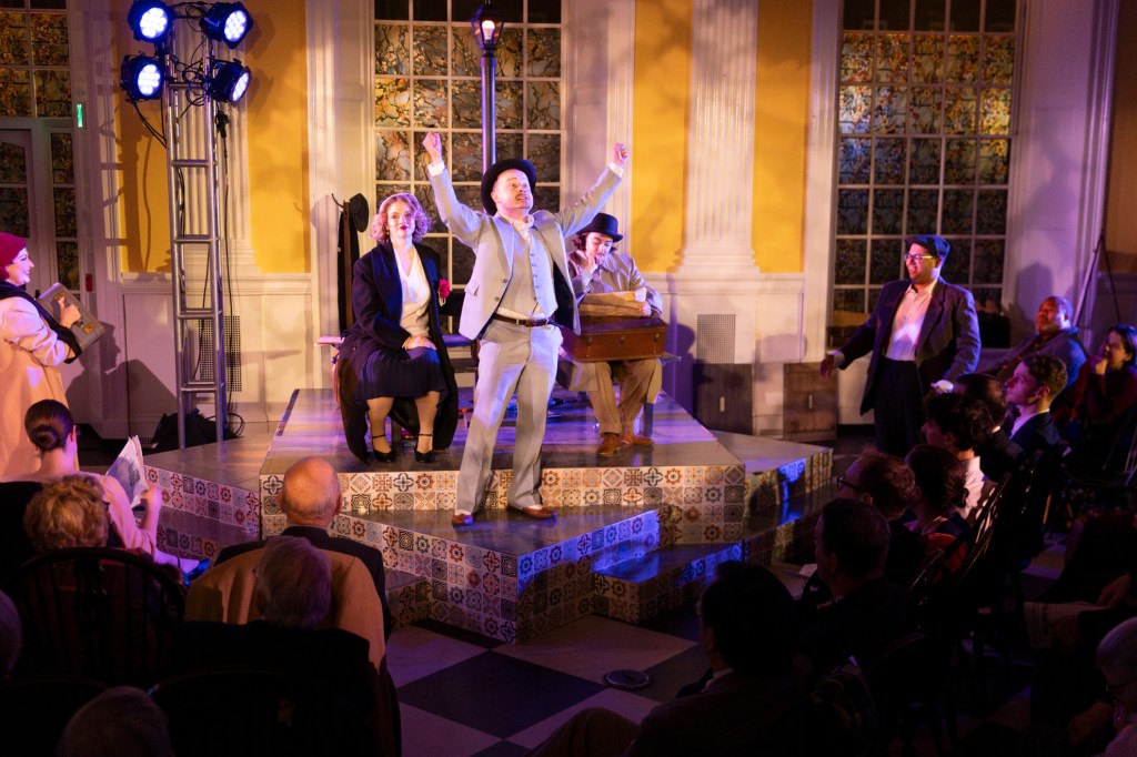 Marcus Schenck raises both arms in the air during a scene in the Lowell House Opera.