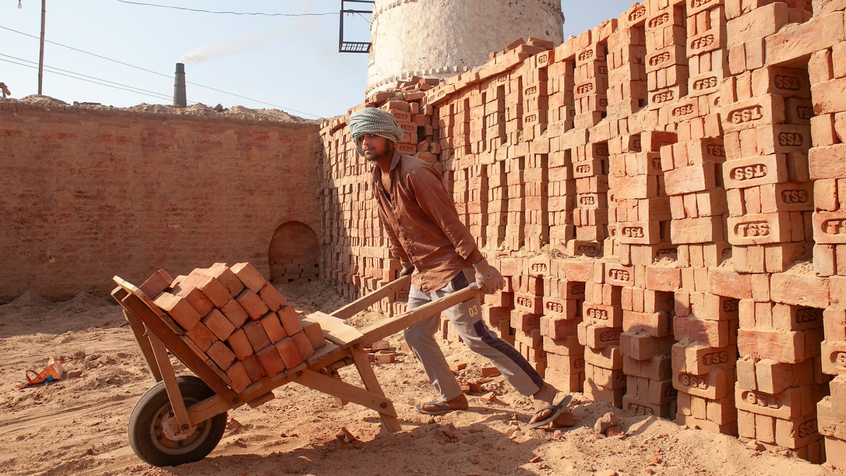 A man wheels bricks from a kiln under intense heat in India.