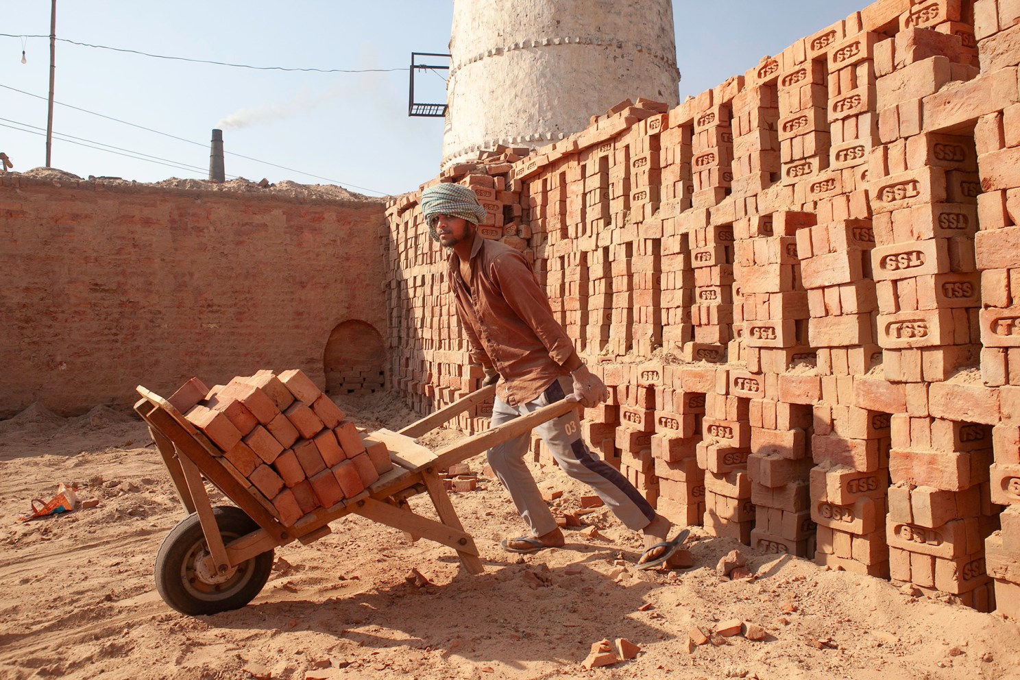 A man wheels bricks from a kiln under intense heat in India.