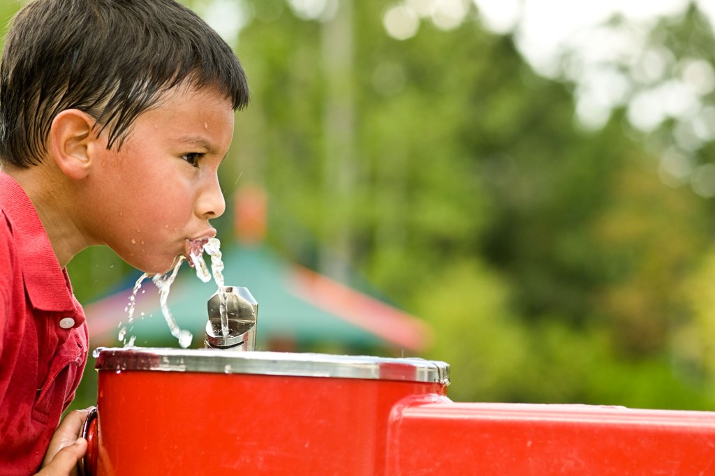Little boy getting heat relief from water fountain.