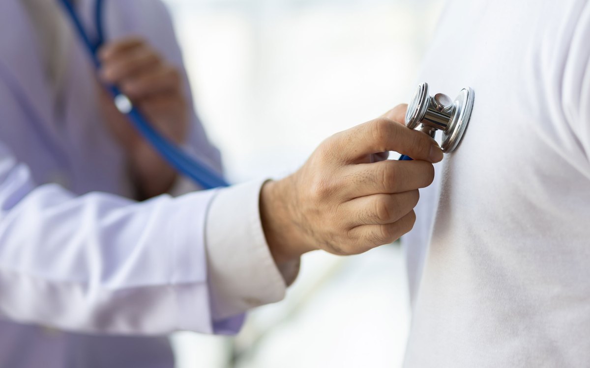 Doctor using stethoscope examining male patient.