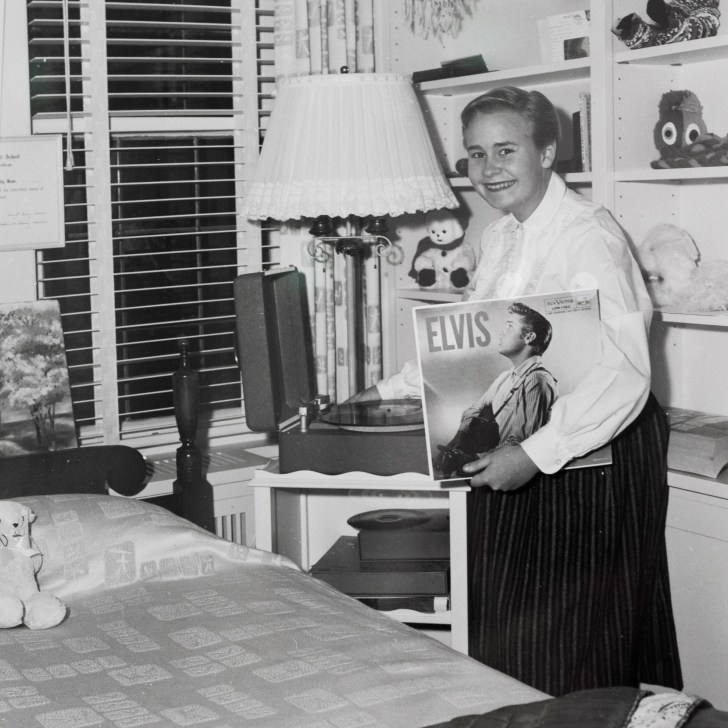 A black and white photograph of a teenage girl holding an Elvis Presley record